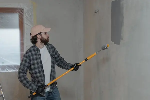 Painter rolling grey paint onto an interior wall in Rochester